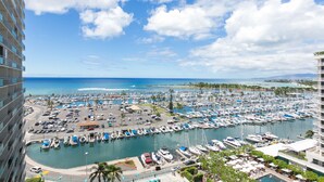A marina with numerous boats docked, a parking area, and a view of the ocean and distant land. - Marina Hawaii Vacations at the Ilikai Tower (Honolulu)