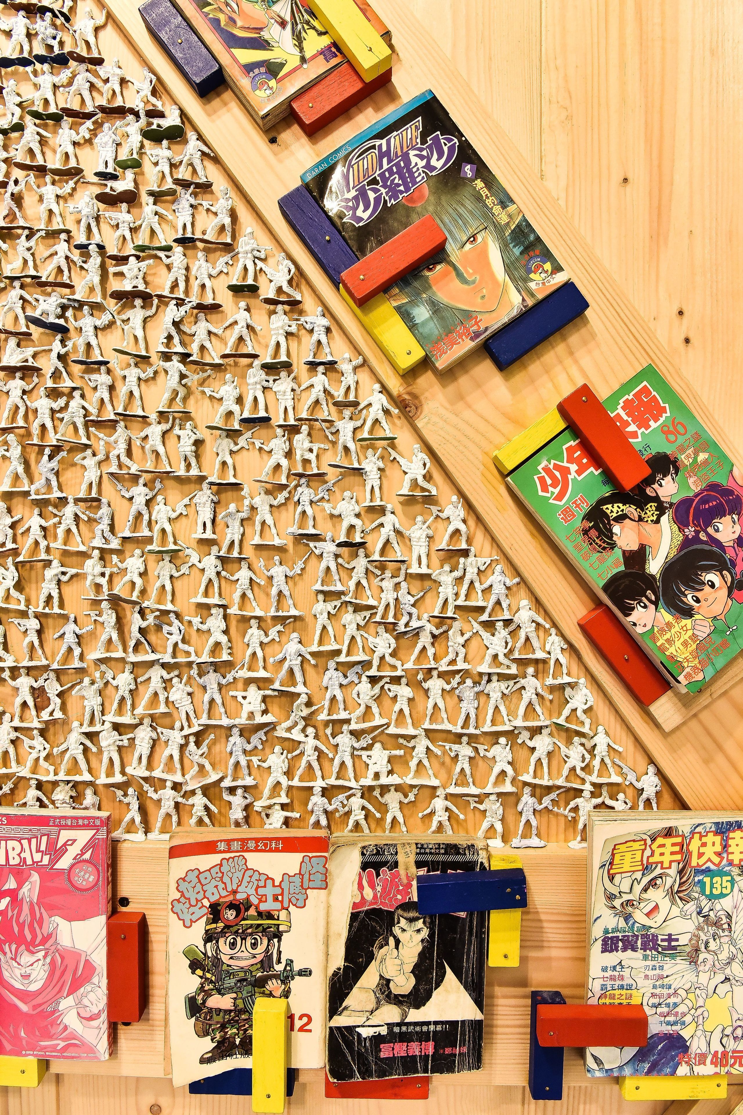 A wooden surface with numerous white figurines arranged in rows, and several manga books placed on it.