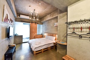 A bedroom with a wooden bed, a TV on a stand, a hanging light fixture, and a clothes rack.