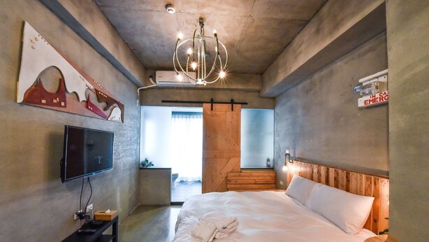 Une chambre d’hôtel moderne dotée d’un grand lit, d’un téléviseur à écran plat, d’un lustre et d’une tête de lit en bois.