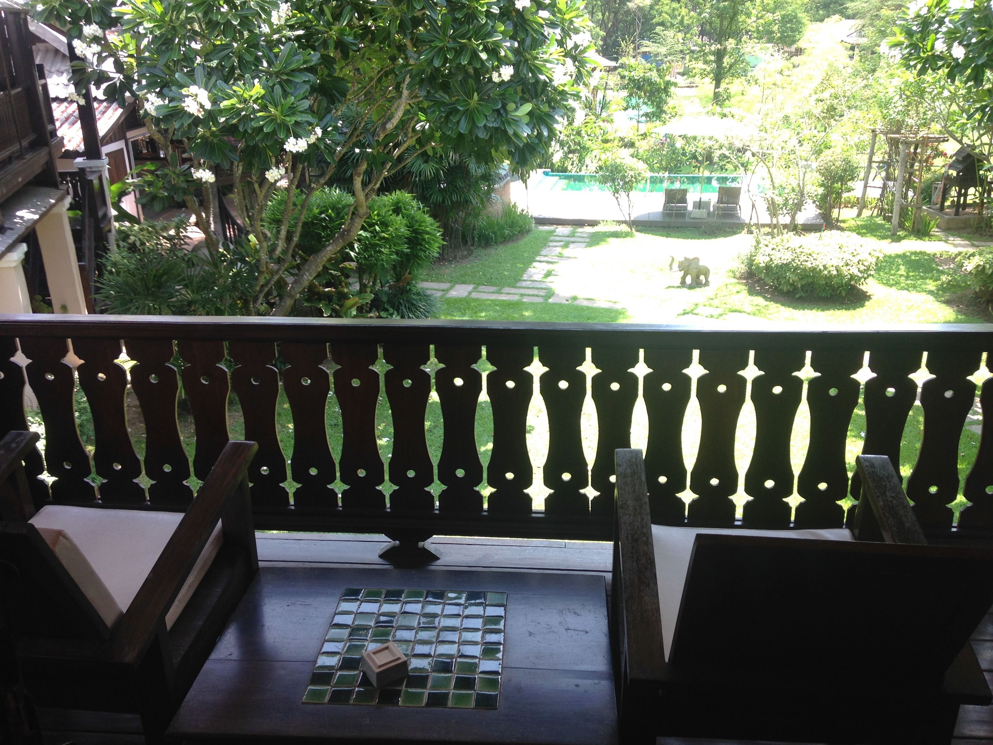 Un balcon donnant sur un jardin, une table carrelée et une chaise en bois.