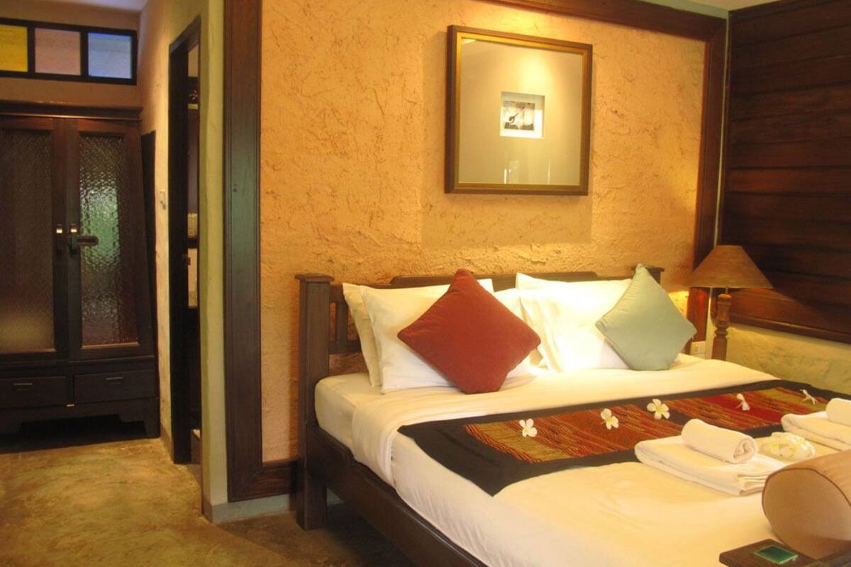 A hotel room with a wooden bed, white linens, a framed picture on the wall, and a wooden wardrobe.