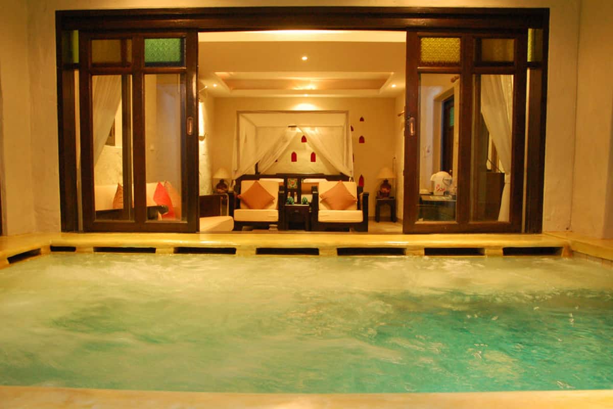 A spa area with a hot tub, a sofa, and a small table with a lamp.