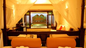 A hotel room with a bed, two pillows, a nightstand, and a window with a view of palm trees and a pool. - Pai River Corner Resort (Pai)