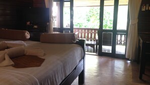 A bedroom with a large bed, a television, and a balcony with a view of greenery. - Pai River Corner Resort (Pai)