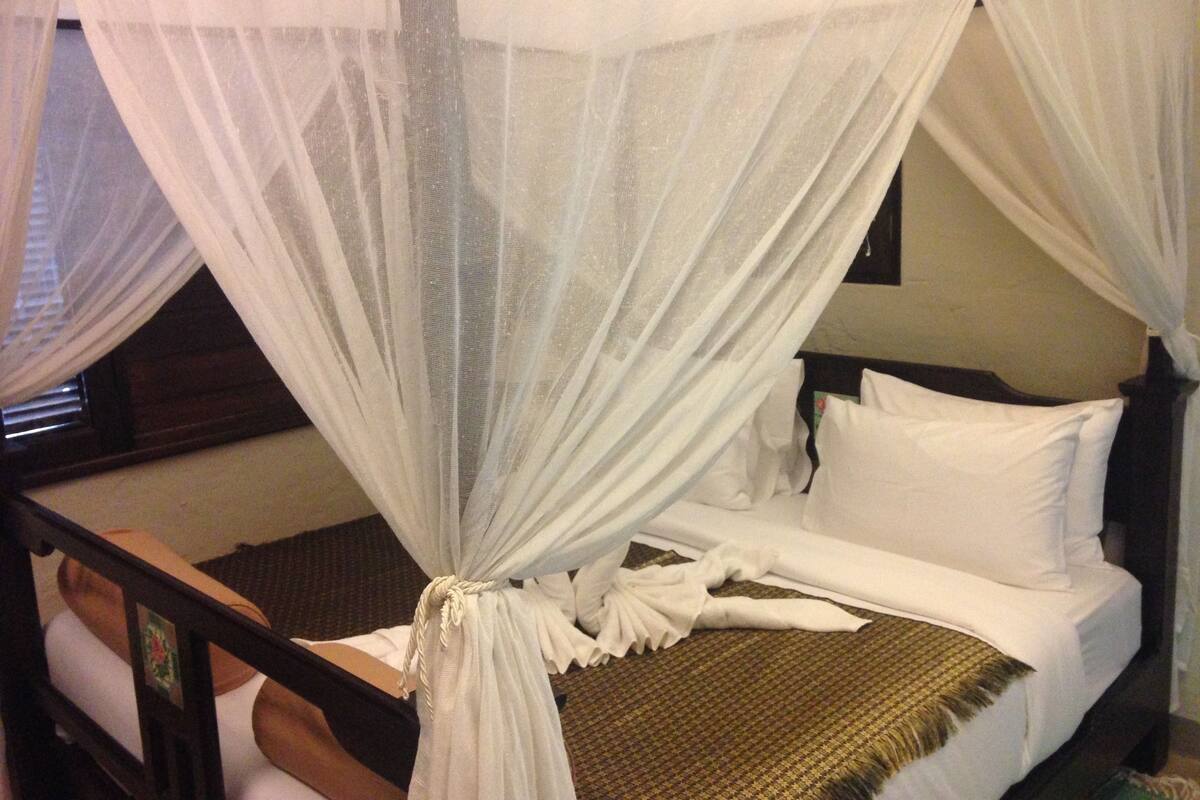 A bed with a canopy, white bedding, and a woven rug.