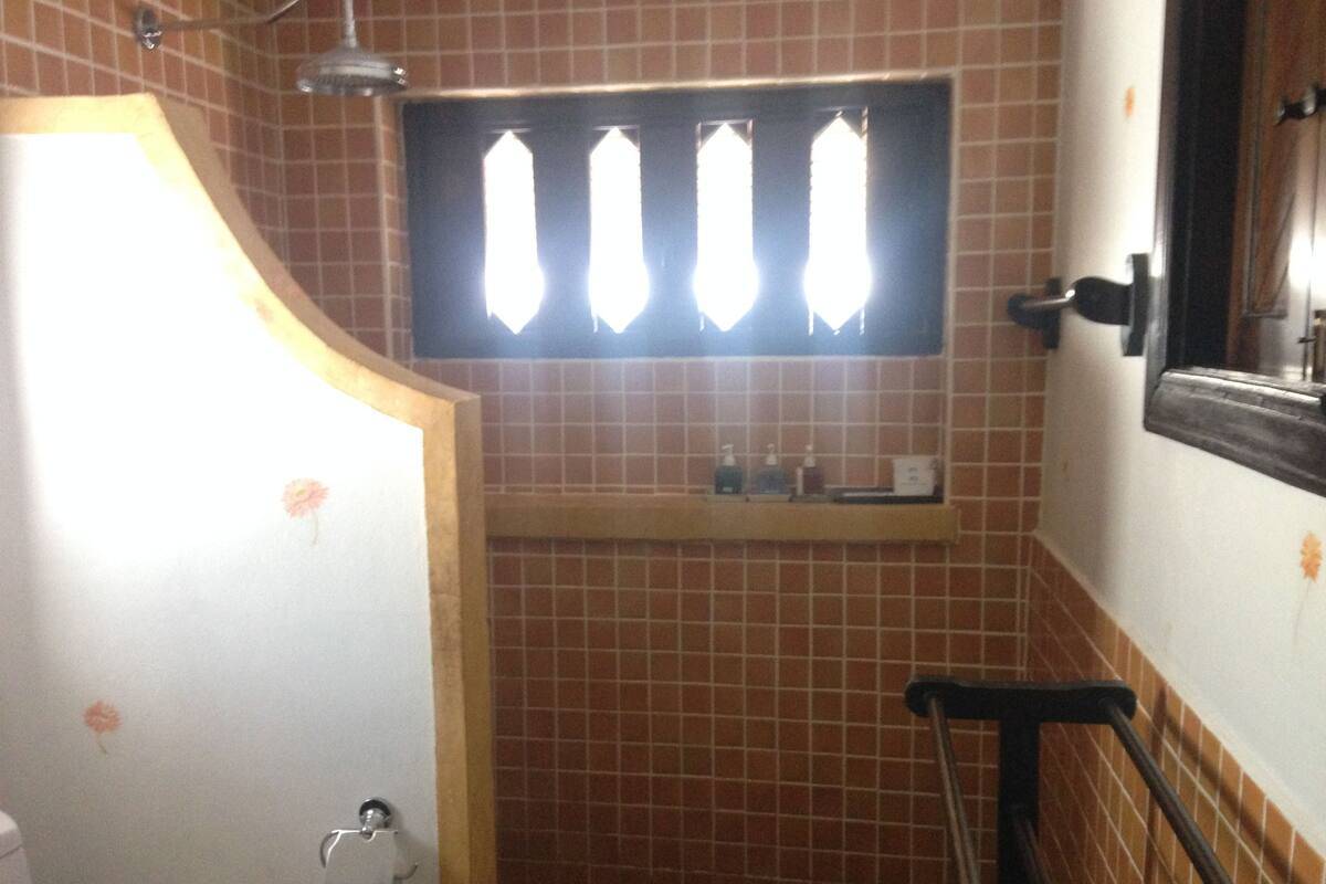 A bathroom with a tiled wall, a shower area, a towel rack, and a window with blinds.