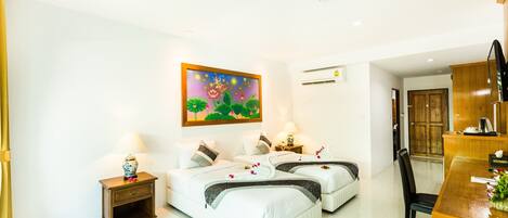 A hotel room with two beds, a desk, a chair, a small table, a painting, and an air conditioning unit.