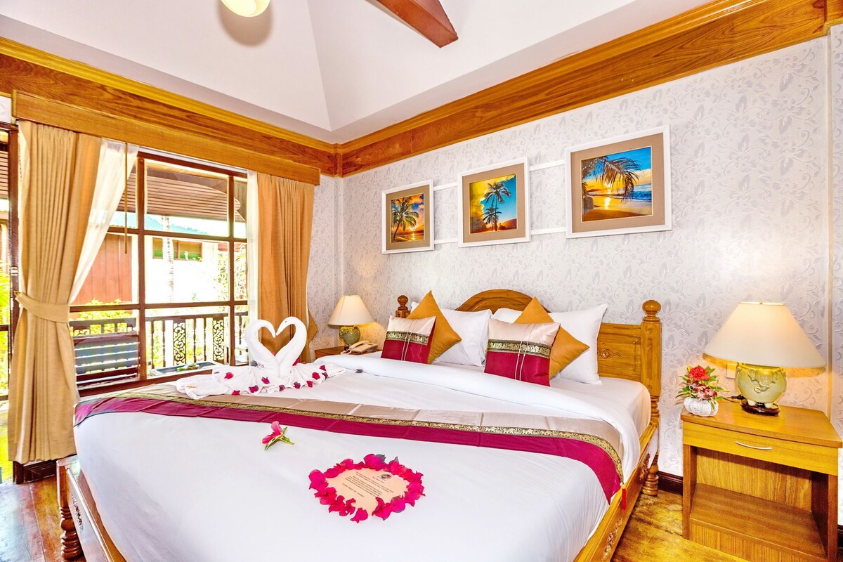 A hotel room with a large bed, wooden headboard, a window with curtains, and wall-mounted artwork.
