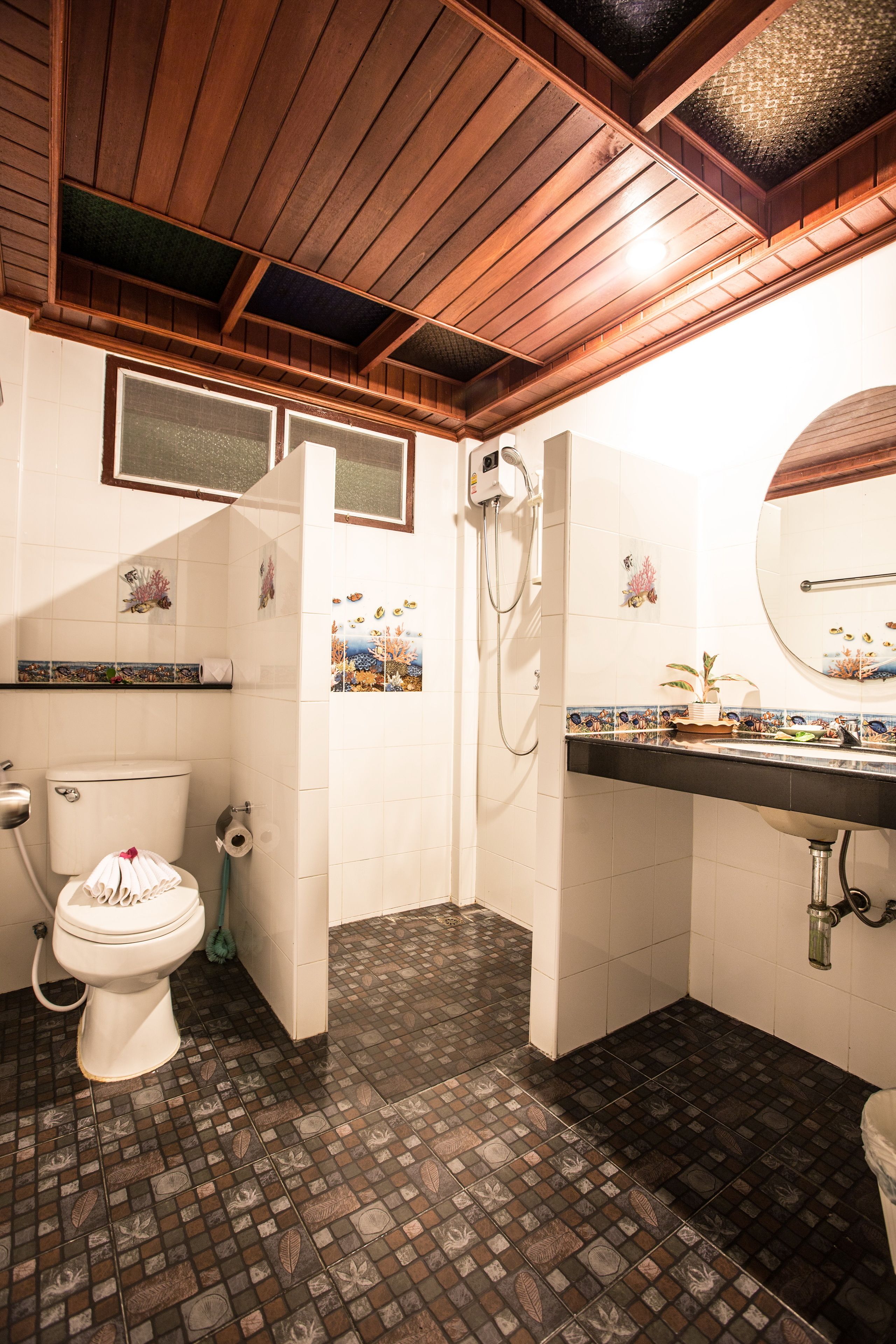 A bathroom with a wooden ceiling, a toilet, a shower, and a sink with decorative tiles.
