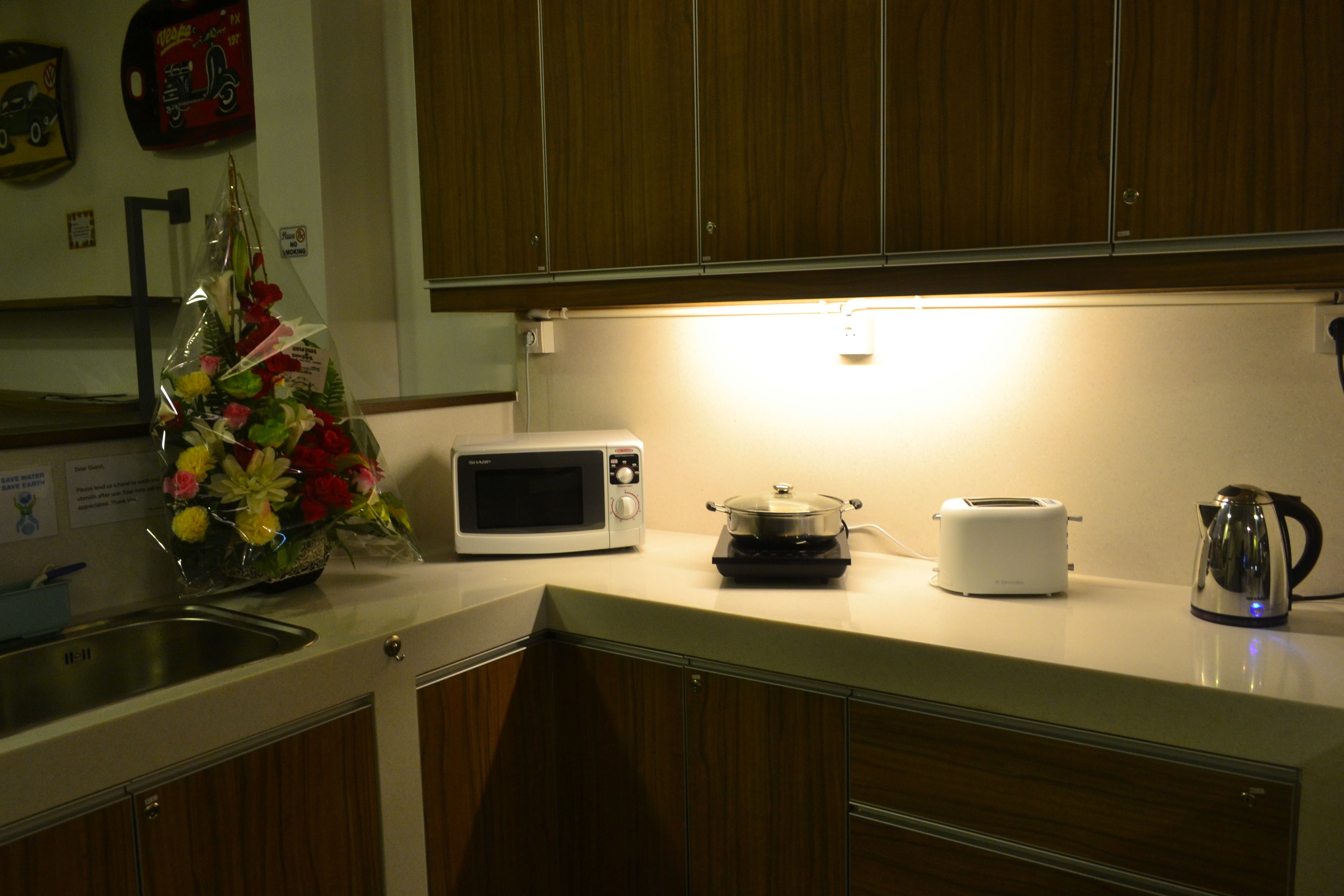 A kitchen with wooden cabinets, a microwave, a toaster, a kettle, and a bouquet of flowers on the counter.