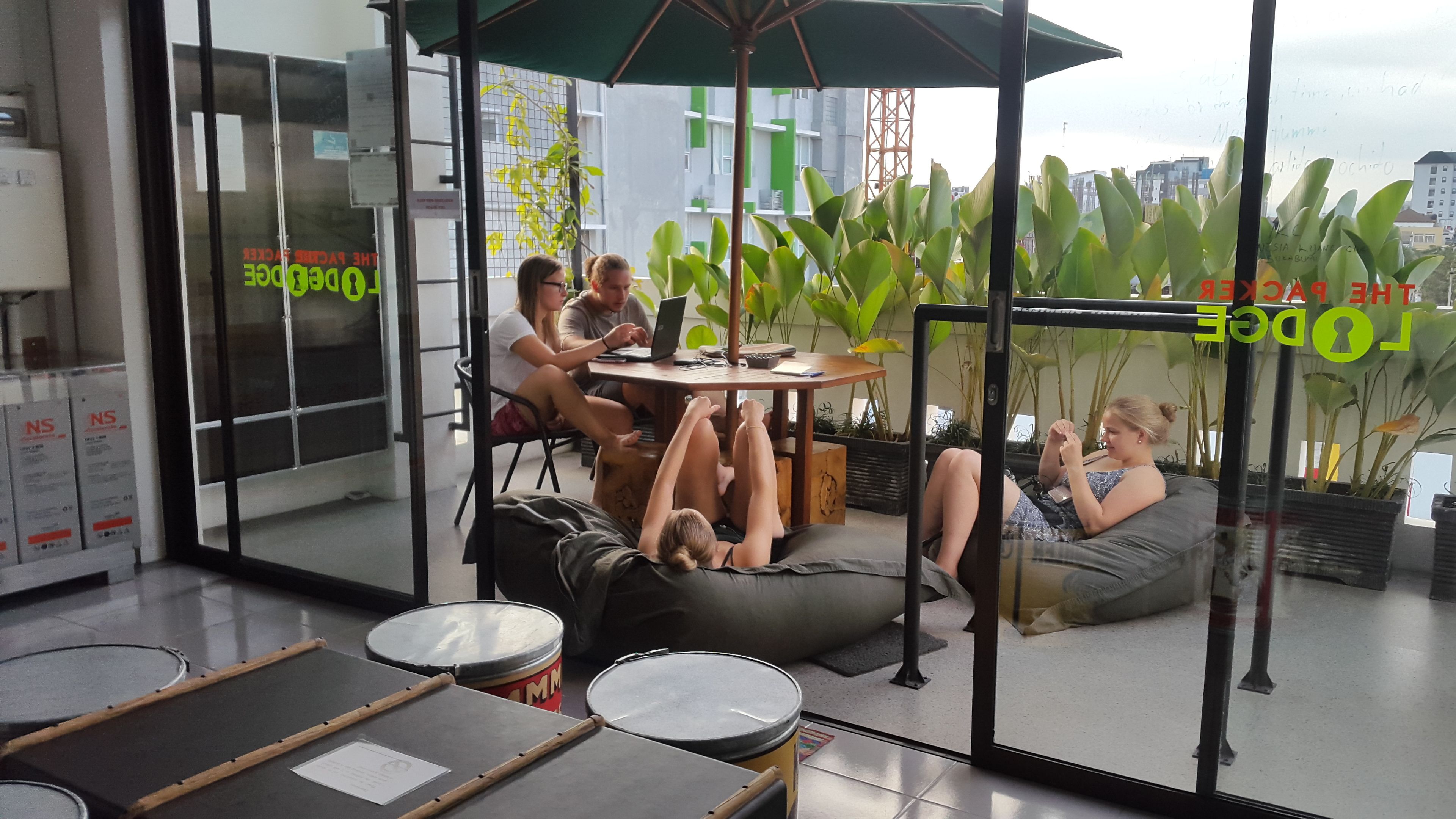 A modern office space with a glass partition, a round table with a laptop, and a person lying on a bean bag chair.