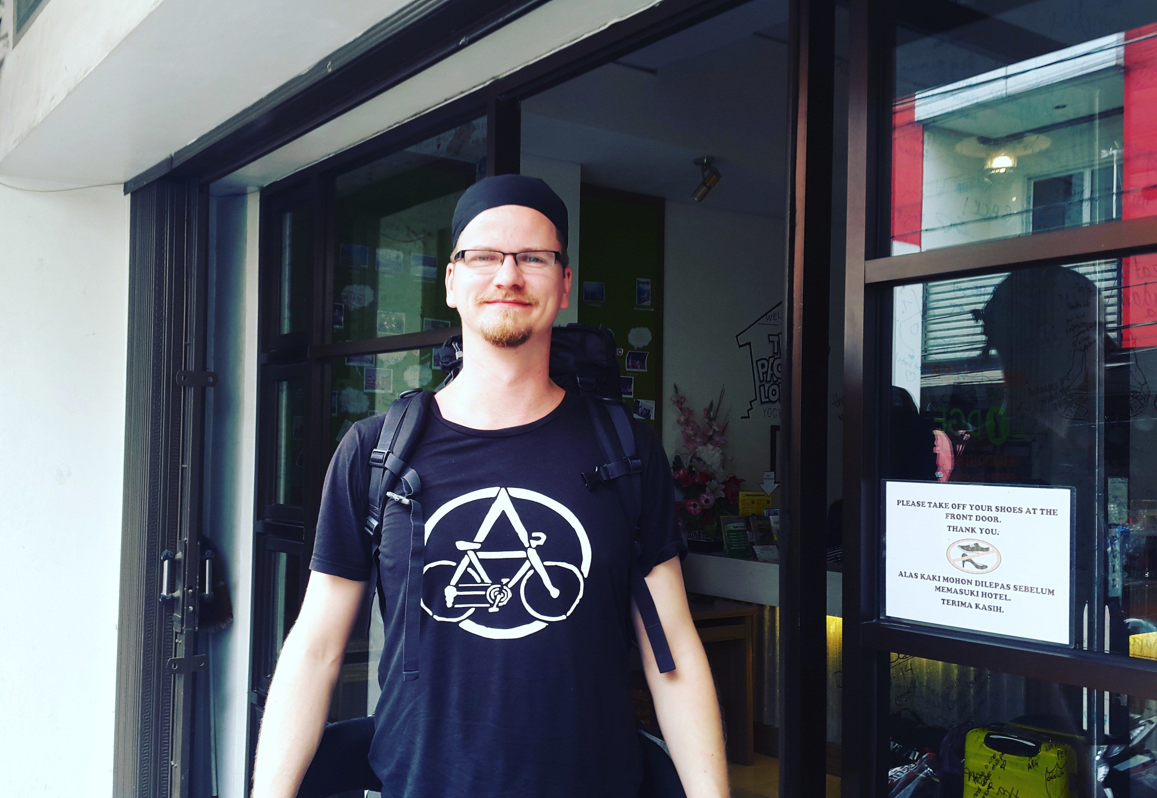 Una persona in piedi di fronte a un edificio con un cartello che invita gli ospiti a togliersi le scarpe all'ingresso.