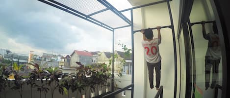 A person hanging from a pull-up bar on a balcony with a city view.