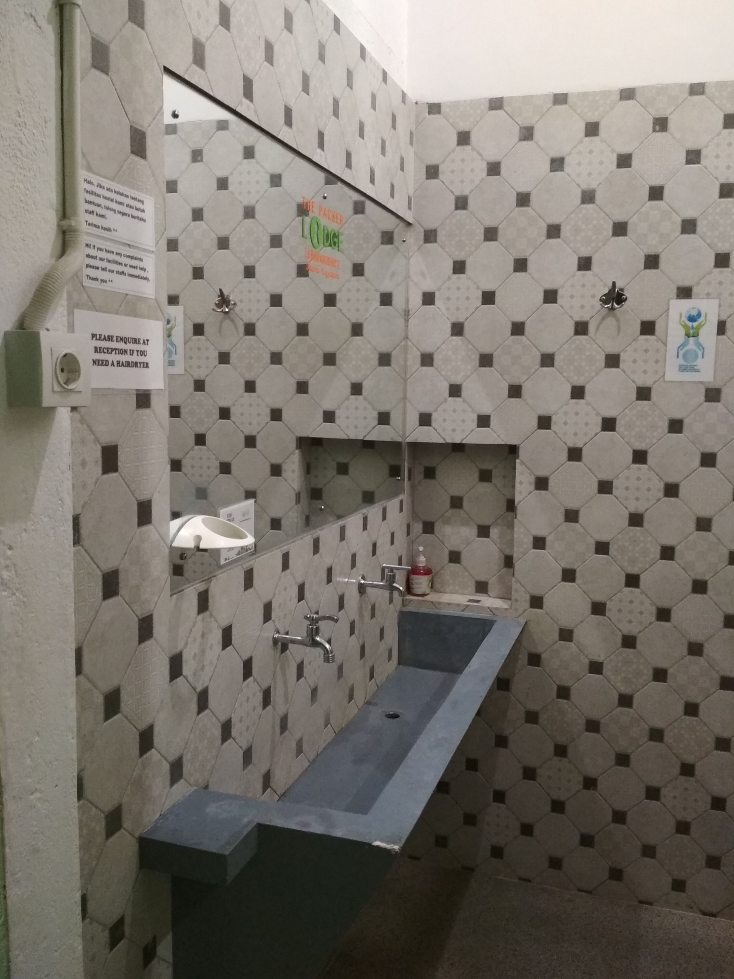 Ein Badezimmer mit sechseckischem Fliesenmuster, einem Spiegel, einem Waschbecken und einem Schild, das darauf hinweist, dass ein Föhn an der Rezeption erhältlich ist.