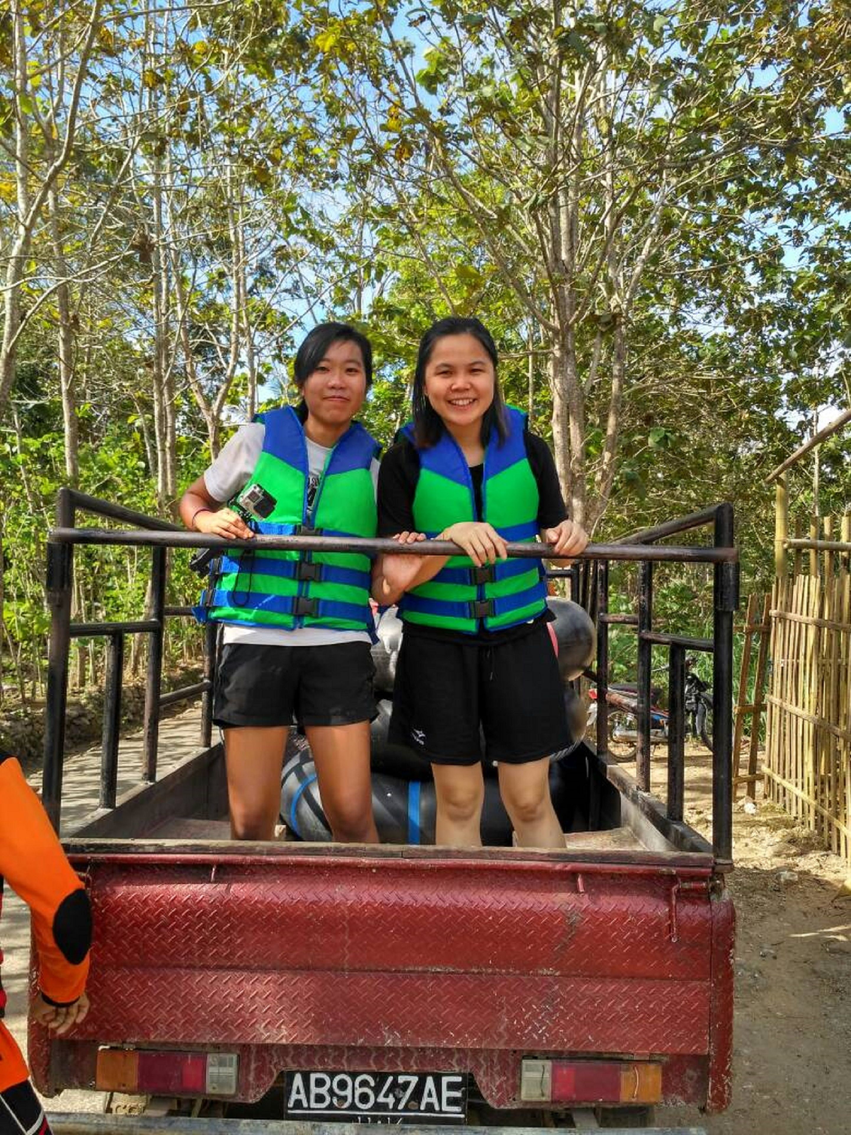 Two people in a truck bed with a metal railing, surrounded by trees.