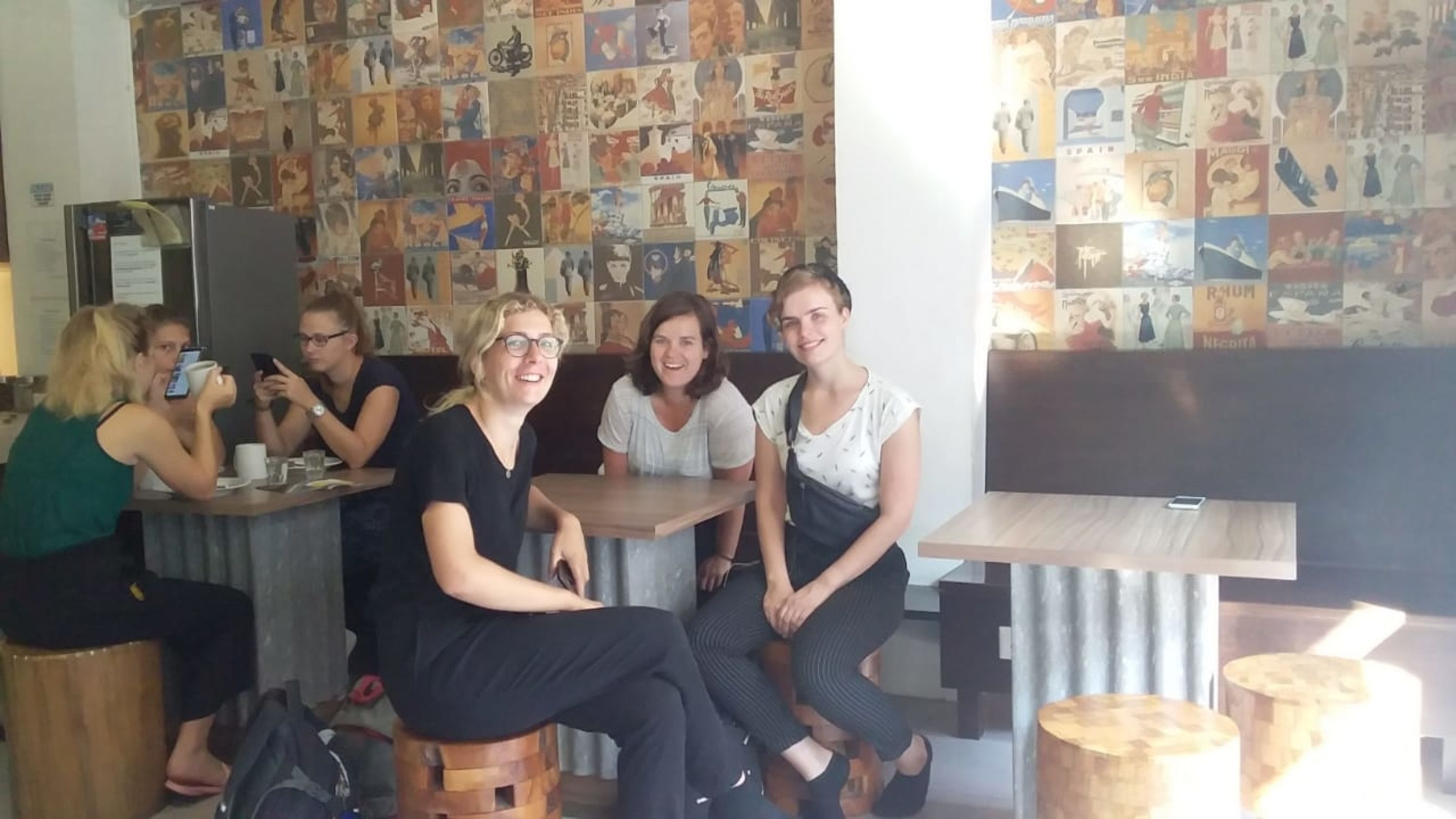 A group of people seated at a counter in a cafe with a wall decorated with various posters.