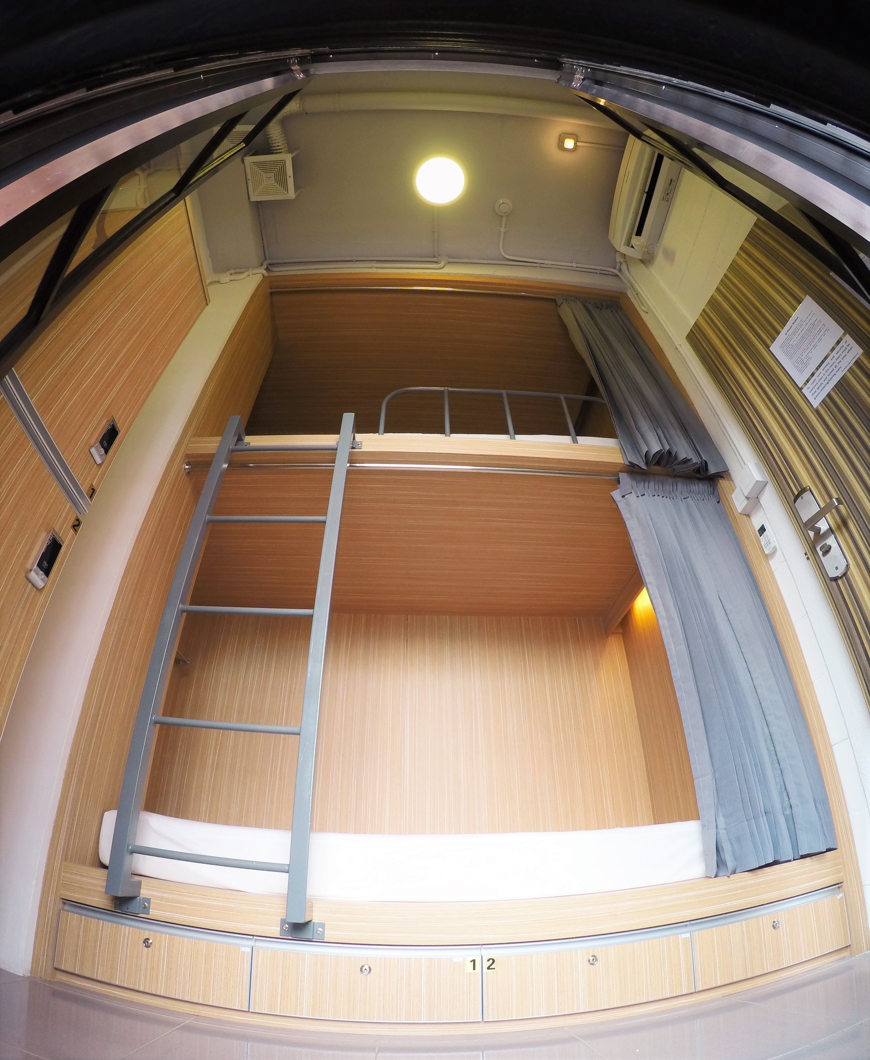 A compact, well-lit room with a bunk bed, wooden paneling, and a small window.