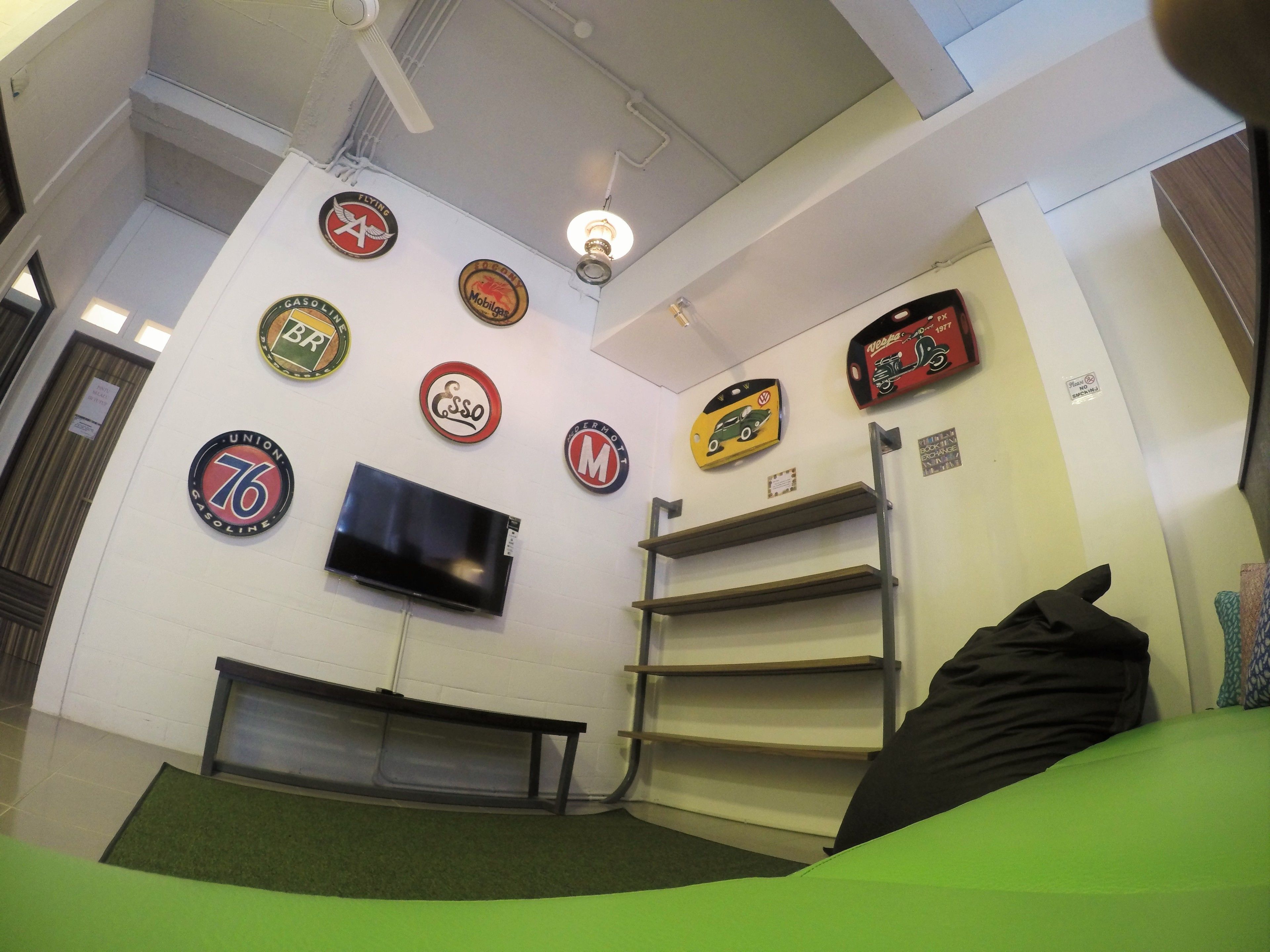 A room with a TV mounted on the wall, a ceiling fan, and various car brand logos on the wall.
