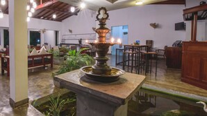 A spacious indoor area with a central water feature, seating arrangements, and a ceiling with exposed beams and hanging lights. - Hotel Wewa Addara (Sigiriya)