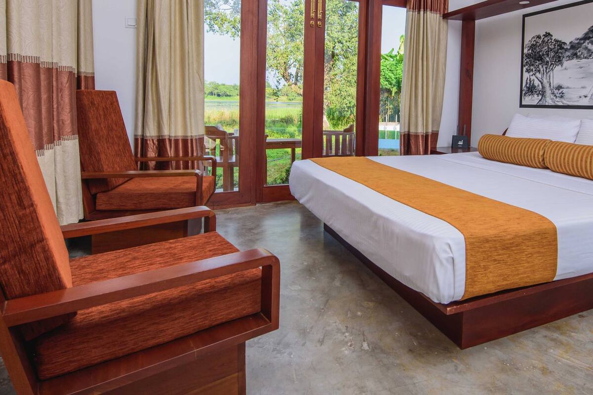 A hotel room with a wooden bed, a wooden chair, a desk, and a view of the outdoors.