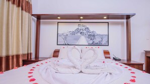 A hotel room with a bed, a painting on the wall, and a wooden desk. - Hotel Wewa Addara (Sigiriya)