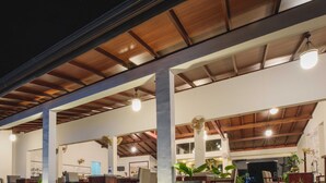 A covered outdoor area with multiple seating arrangements, including tables and chairs, and a staircase leading to an upper level. - Hotel Wewa Addara (Sigiriya)