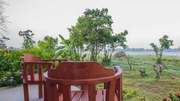 A wooden bench and table set on a concrete surface with a view of a grassy field and trees.