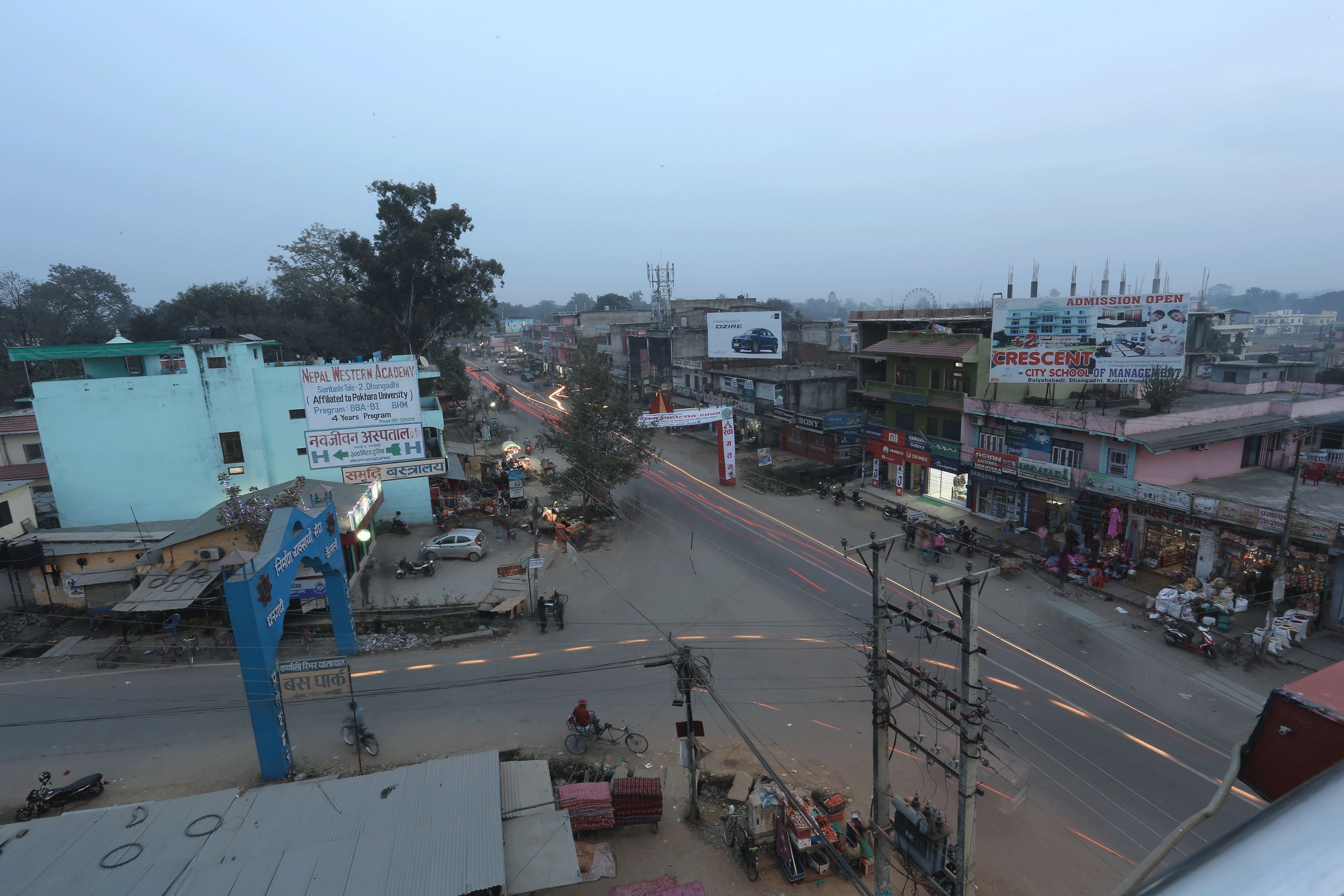 Vista de la calle con edificios, un letrero de Nepal Western Academy y un anuncio publicitario de Crescent City School of Management.