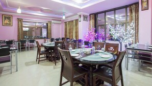 A dining area with round tables and chairs, a large window with curtains, and a ceiling with recessed lighting. - Hotel Jalsa (Dhangadhi)