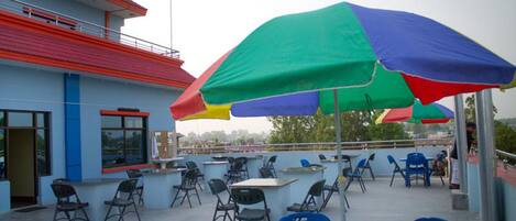 An outdoor seating area with tables and chairs, umbrellas, and a building with a red roof.
