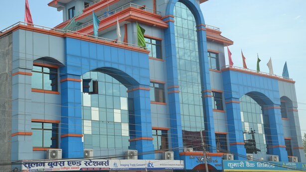 A modern building with blue and orange architecture, featuring large windows and multiple flags. - Hotel Jalsa (Dhangadhi)