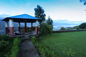 A gazebo with a blue roof, surrounded by greenery and a view of distant mountains.