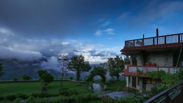A two-story stone building with a red roof and a balcony, surrounded by lush greenery and a river. - Dhaulagiri View Hotel (Pokhara)