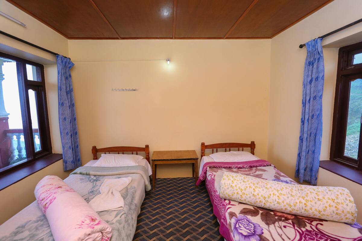 A room with two single beds, a small wooden table, and a window with curtains.
