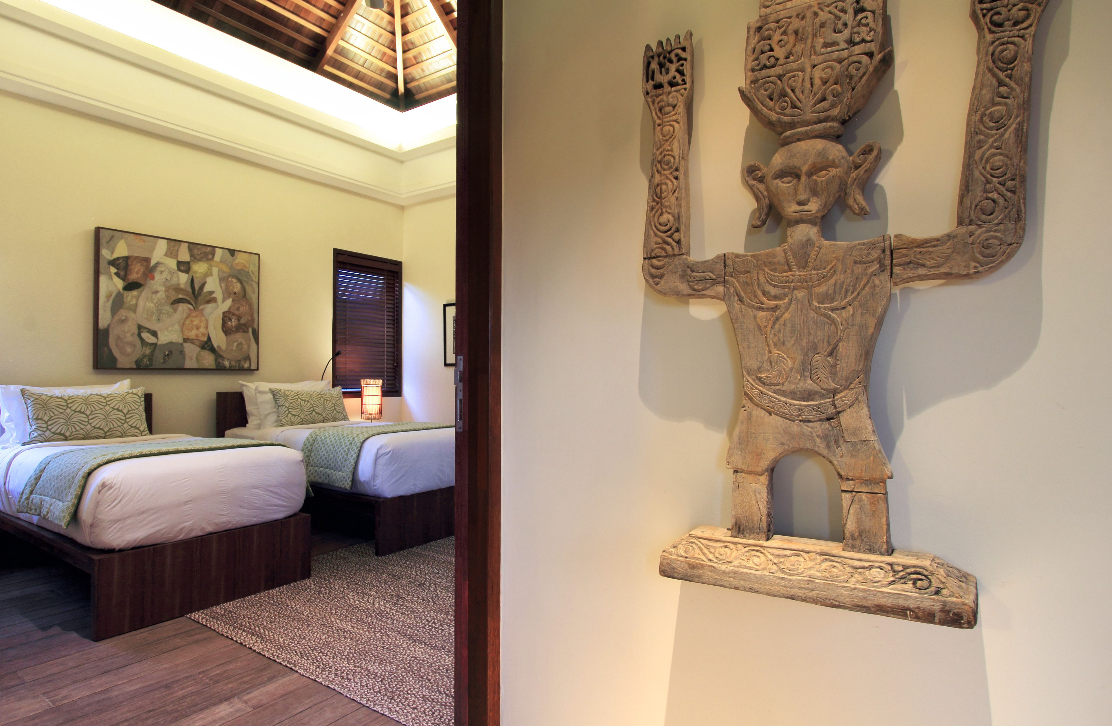 A bedroom with two beds, a wooden headboard, a large painting, and a wall-mounted sculpture.