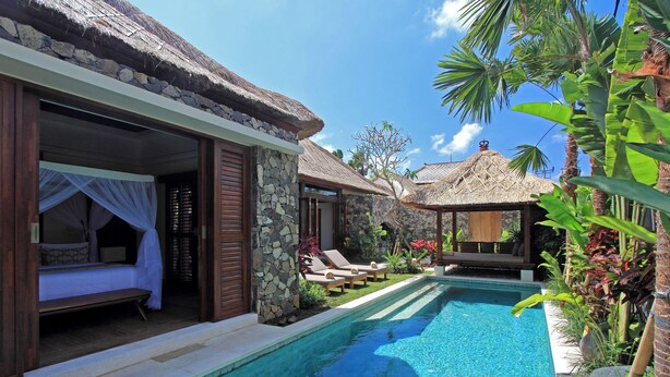 A poolside area with a bed, lounge chairs, and a thatched-roof structure. - Villa Suar Drupadi (Seminyak)