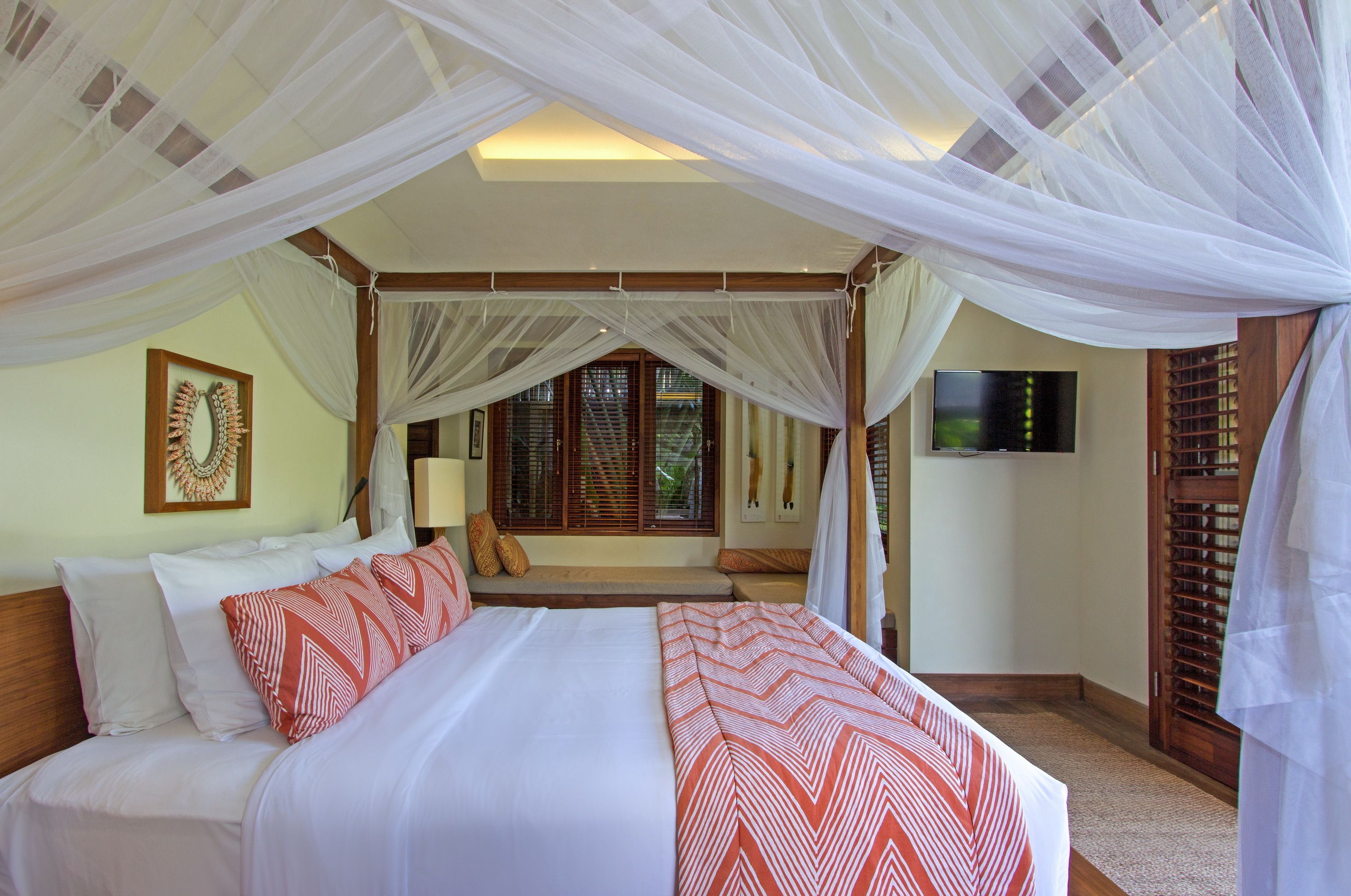 A bedroom with a canopy bed, a television, and a window with wooden shutters.