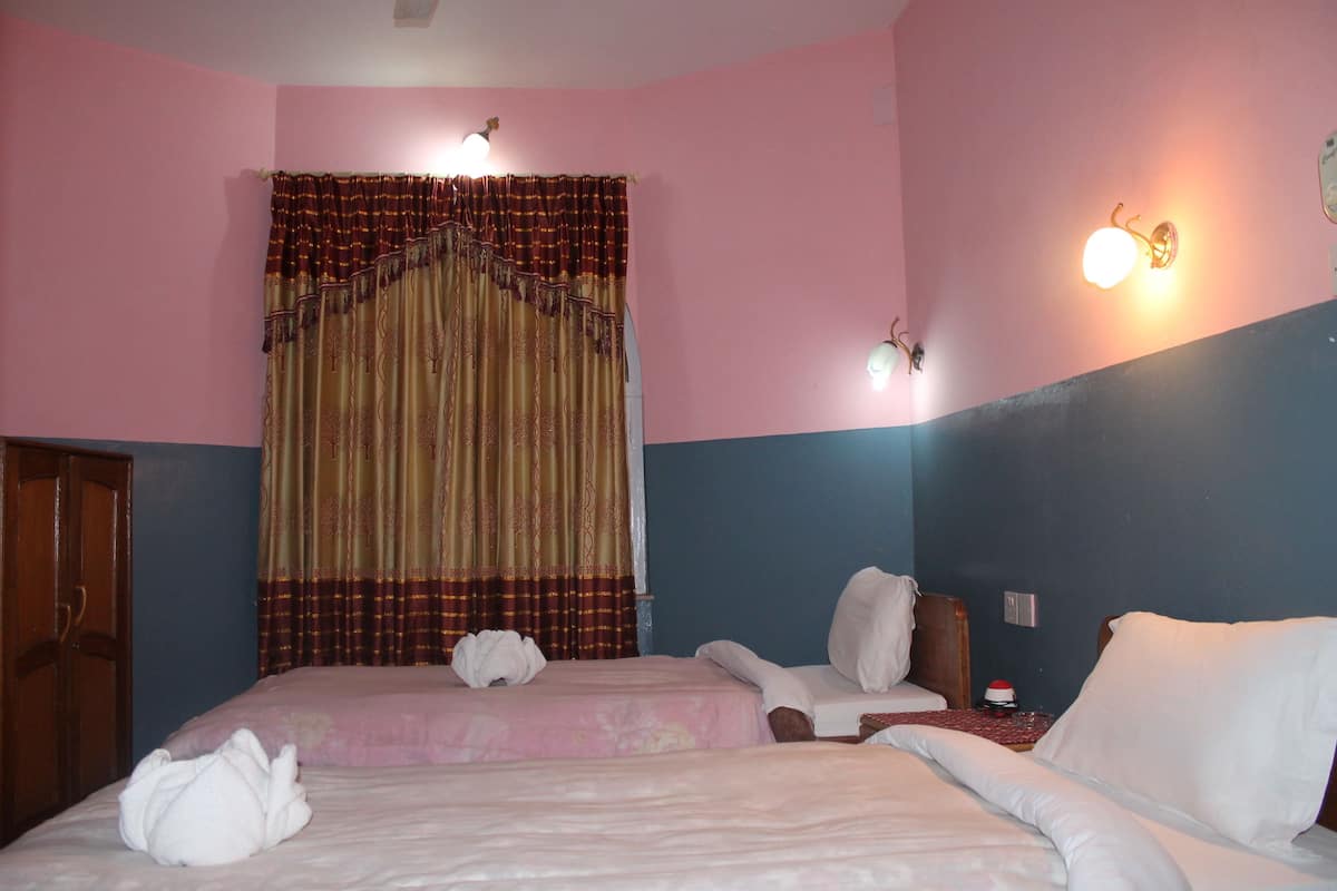Una habitación de hotel con una cama, dos mesitas de noche, una puerta de madera y una cortina.