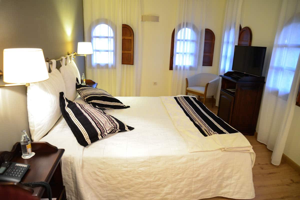 Ein Hotelzimmer mit einem Bett, einem Schreibtisch mit Telefon, einem Fernseher und einem Sessel.