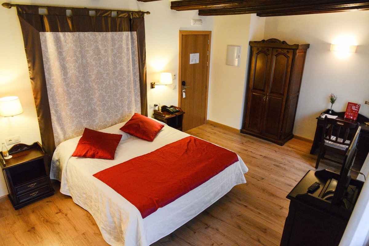Ein Hotelzimmer mit Bett, Holzschrank, Nachttisch, Lampe und Fernseher.