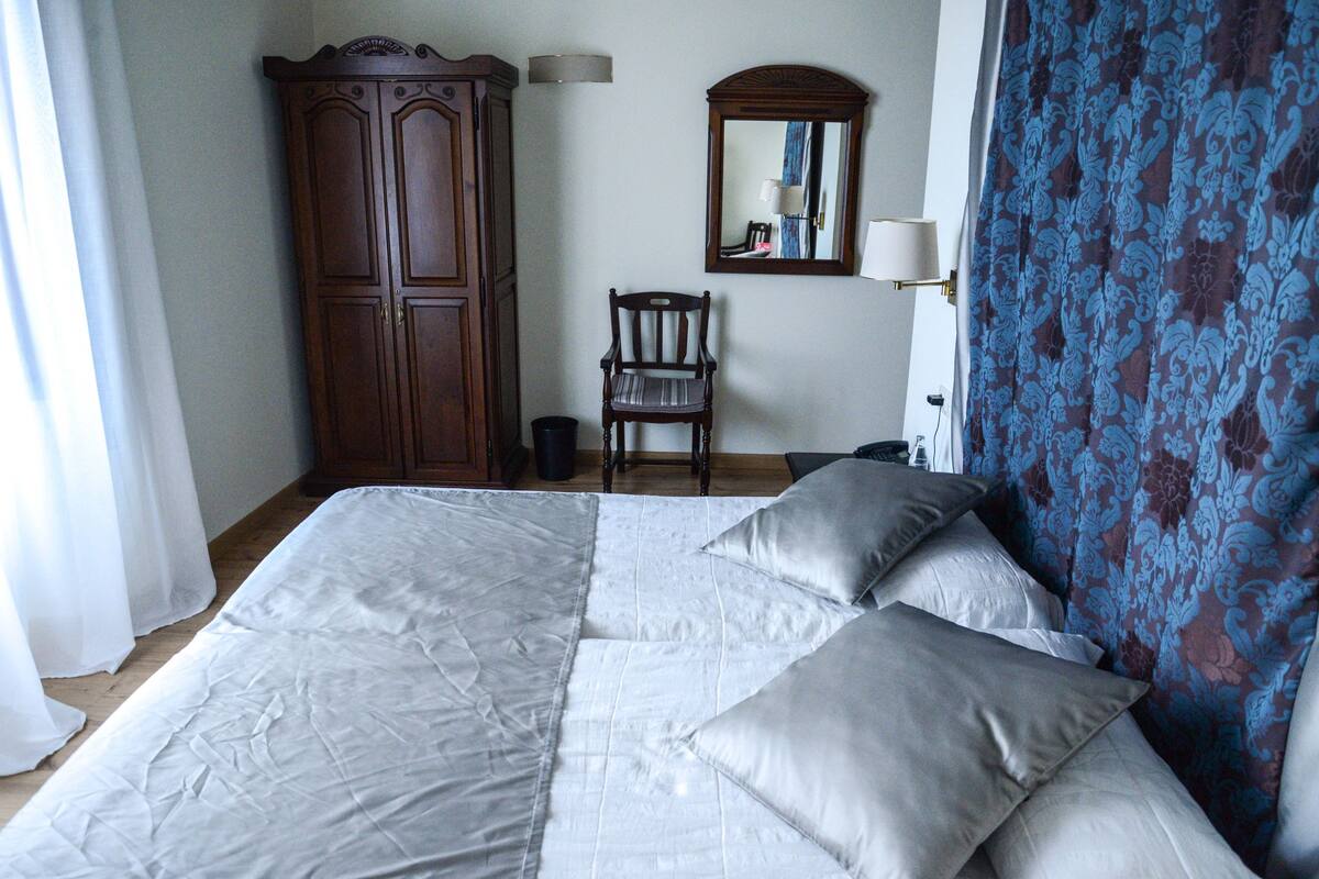 Ein Schlafzimmer mit einem großen Bett, einem Holzschrank, einem Sessel und einem Spiegel an der Wand.