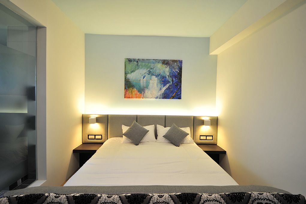 Ein modernes Hotelzimmer mit einem großen Bett, zwei Nachttischen mit Lampen und einem farbenfrohen, abstrakten Gemälde darüber.