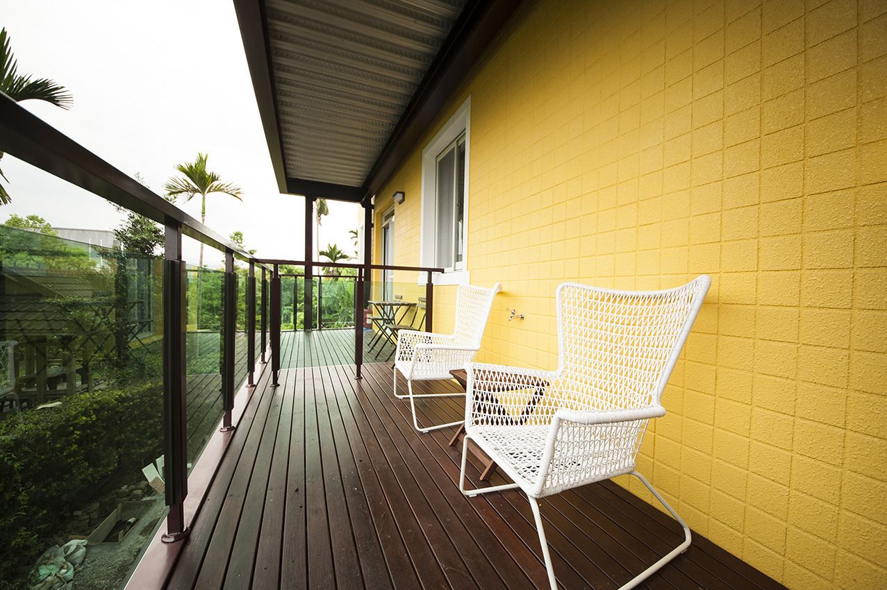 Un balcón con suelo de madera y sillas de metal blanco, con vistas a una zona verde exuberante.