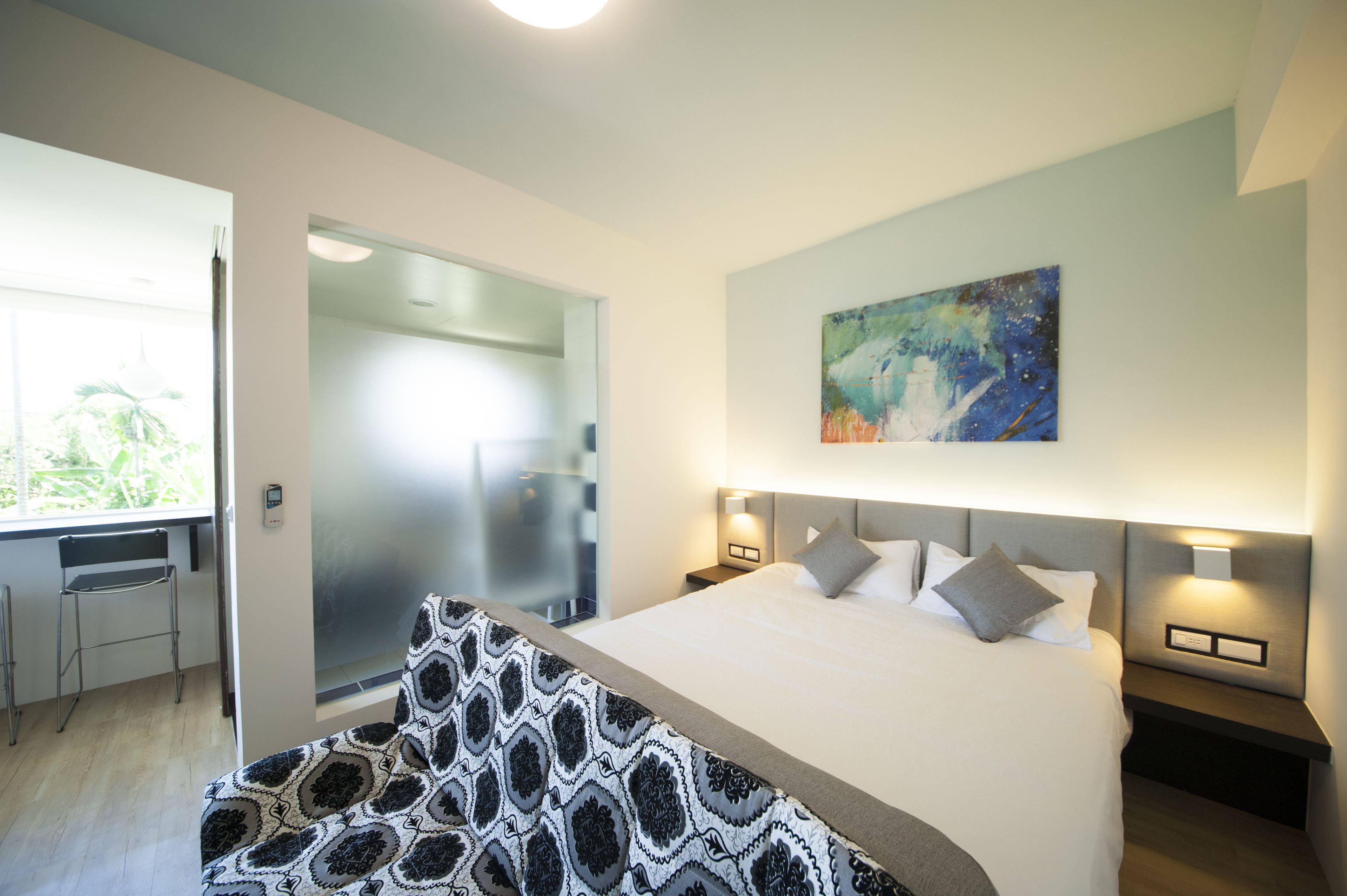 Een moderne hotelkamer met een groot bed, twee nachtkastjes met lampen, een schilderij aan de muur en uitzicht op het landschap door een glazen deur.
