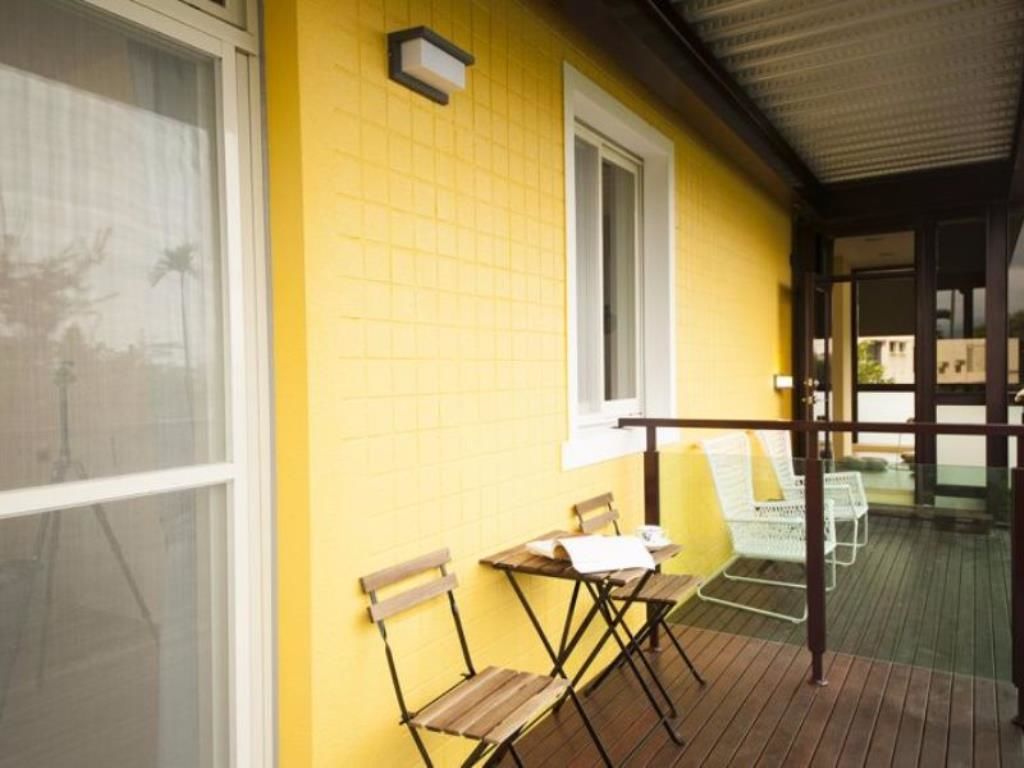 A yellow building with a covered outdoor area, two wooden chairs, and a table.