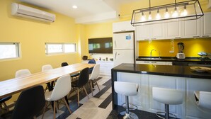 Una cocina moderna con zona de comedor, que incluye una mesa de madera larga, sillas blancas, una isla de encimera negra con taburetes y armarios blancos.