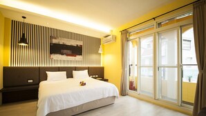 Una habitación de hotel moderna con una cama grande, un televisor montado en la pared, una mesita de noche y un ventanal corredero a un balcón.