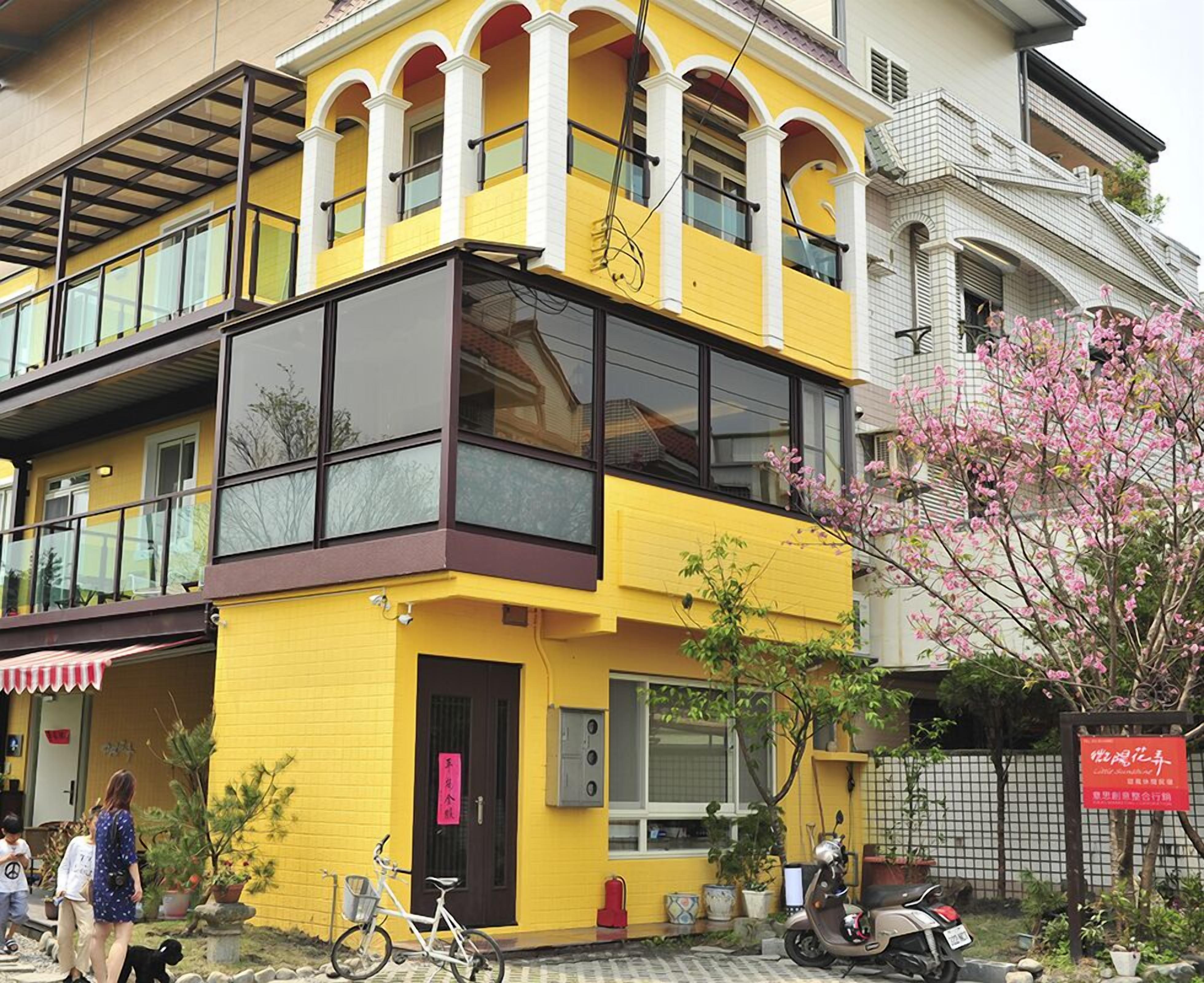 A two-story building with a yellow facade, large windows, and a balcony.