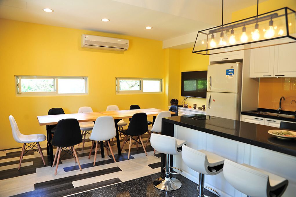 Una cocina moderna con encimera negra, armarios blancos y un refrigerador de acero inoxidable. Cuenta con un comedor con mesa y sillas de madera, y una zona de bar con taburetes.